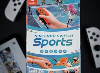 A box of Nintendo Switch Sports is prominently featured, surrounded by various Nintendo Switch controllers and a screen displaying a related interface. The box art depicts animated characters playing sports, such as tennis, with vibrant colors and action-oriented poses.