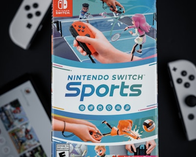 A box of Nintendo Switch Sports is prominently featured, surrounded by various Nintendo Switch controllers and a screen displaying a related interface. The box art depicts animated characters playing sports, such as tennis, with vibrant colors and action-oriented poses.